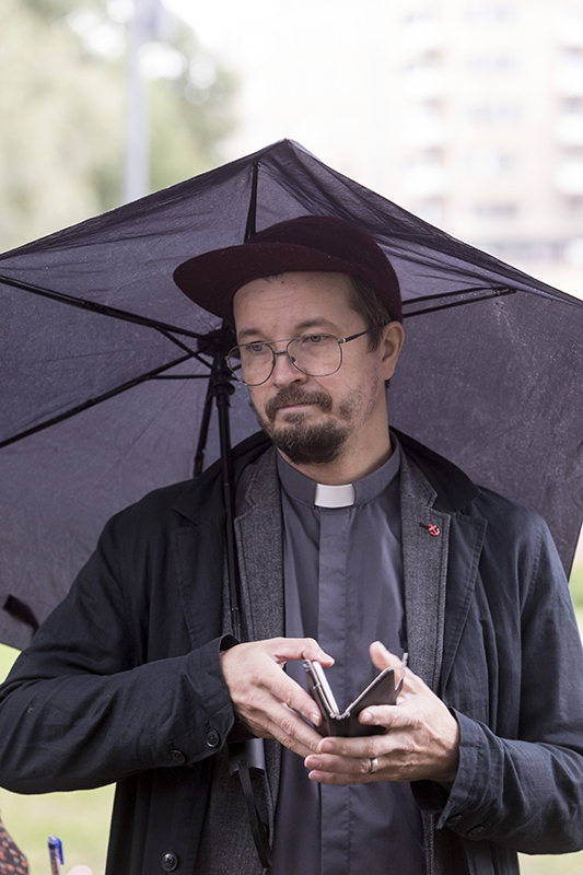Tampereen seurakuntien nuorten aikuisten pappi Olli Viljakainen tumman sateenvarjon alla. Hänellä on mietiskelevä katse suunnattu alaviistoon. Käsissään hän pitelee puhelintaan.