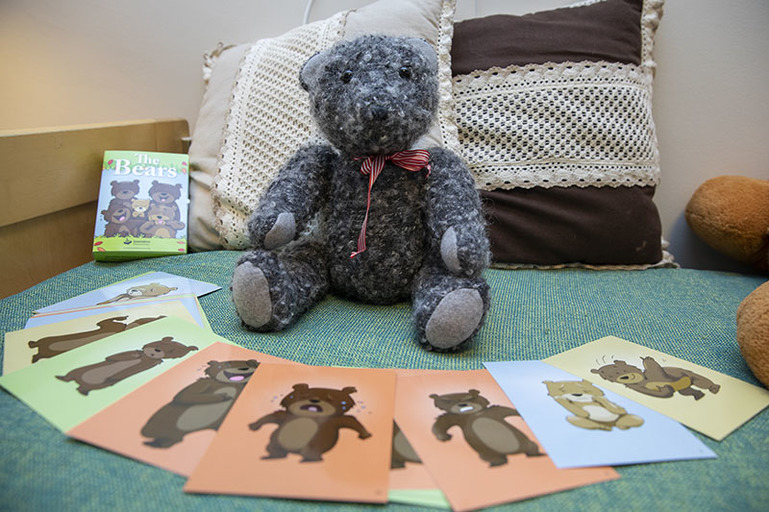 Nalle istuu sängyllä, edessä on nallekortteja puoliympyrässä.