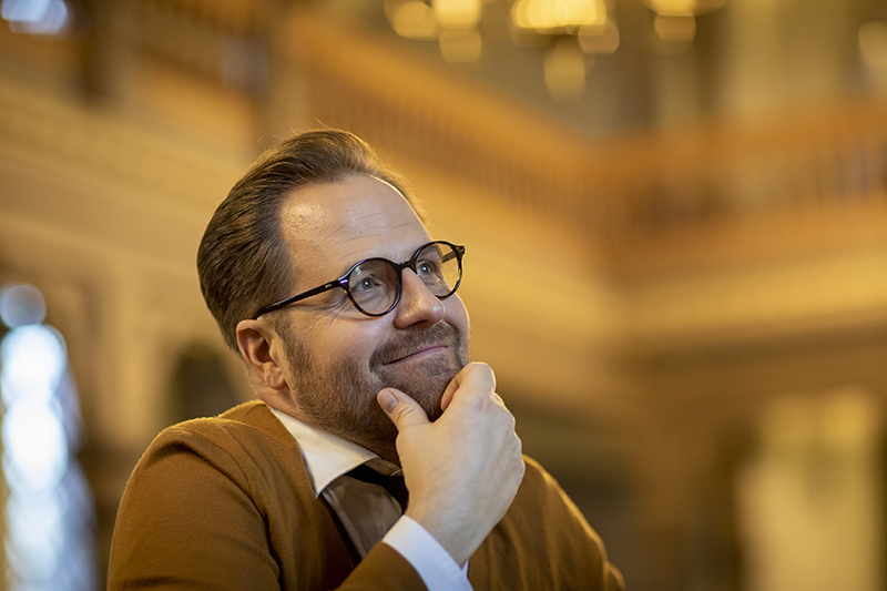 Mies nojaa kättään leuakaan ja näyttää hymyilevän mietteliäältä.