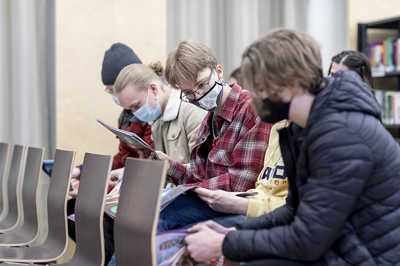 Lukiolaiset nuoret istuvat tuoleilla rivissä ja tutkivat Silta-lehteä. Kaikilla on maskit naamalla.