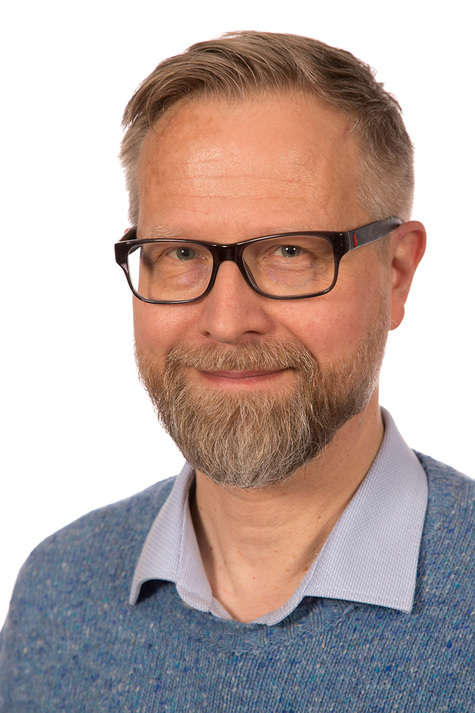 Henkilökuva parrakkaasta miehestä jolla on silmälasit ja sininen neulepaita.