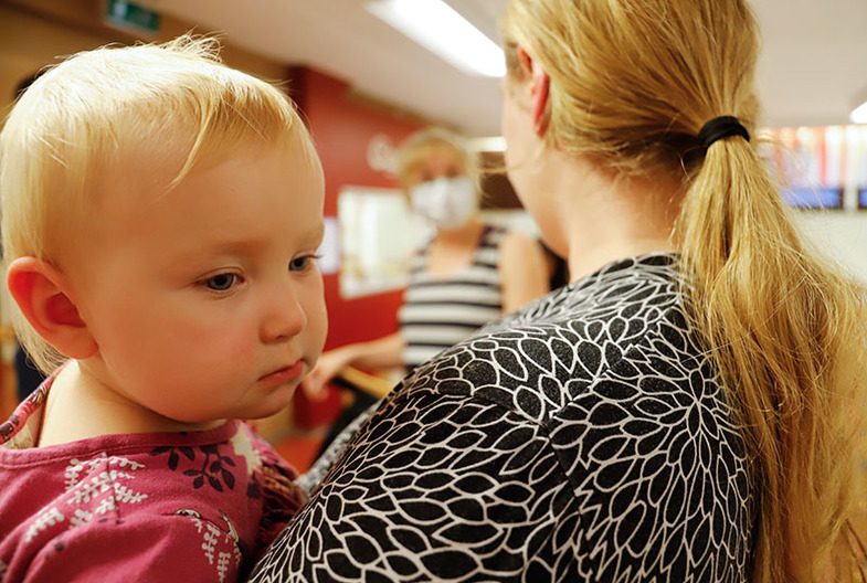 Pieni lapsi naisen sylissä, katsoo naisen olkapään yli. Nainen juttelee taustalla olevan toisen naisen kanssa.