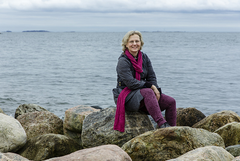 Nainen istuu rantakivillä, ja vettä on laajasti joka puolella.