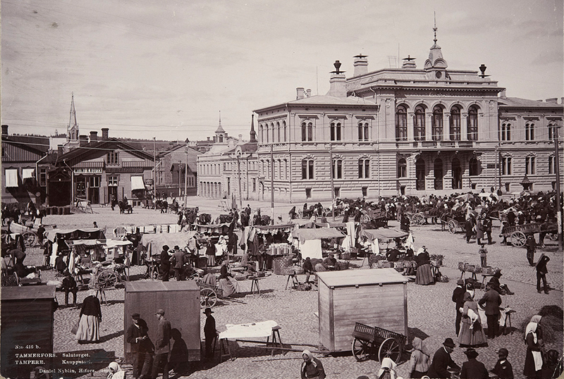 Toripäivän tunnelmaa vuodelta 1893. Paljon ihmisiä ja myyntikojuja jykevän rakennuksen edessä.