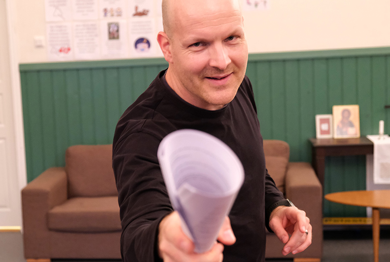 Henkilö osoittaa innokkaana rullalla olevaa paperipinoa kohti katsojaa.