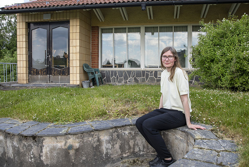 Hymyilevä henkilö istuu ulkona kivisellä kaiteella, ja taustalla on rakennus.
