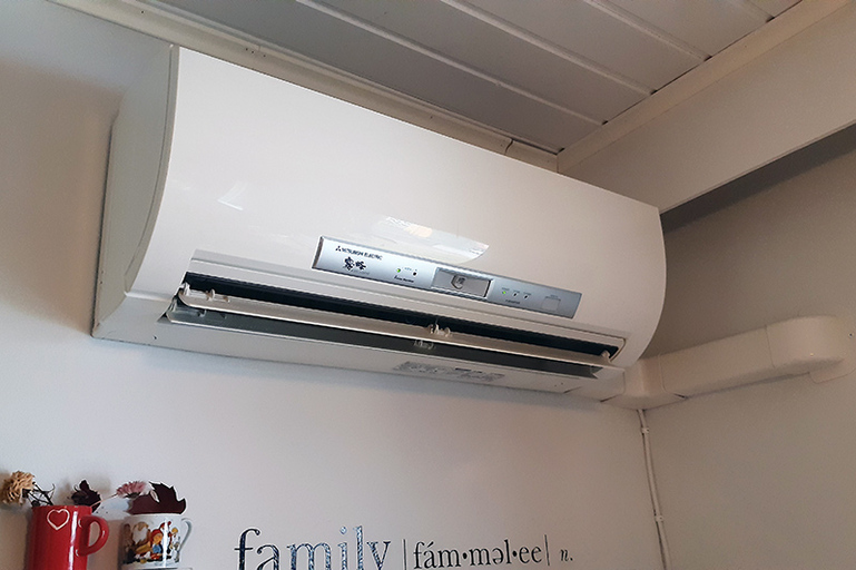 Ilmalämpöpumpun alla seinässä on sisustustekstiä, ja alla vasemmalla kuivakukkia pienissä kipoissa.