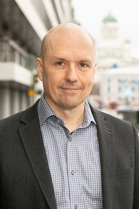 Henkilökuvassa kaljumies katsoo kameraan päin ja hymyilee.