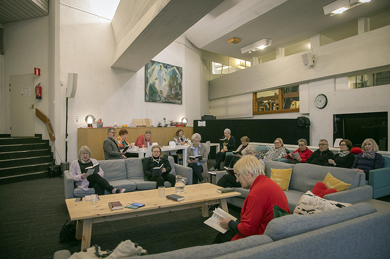 Ihmisiä istuu avarassa tilassa sohvilla selaillen kirjoja.