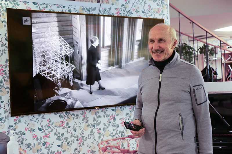 Henkilö kaukosäädin kädessä television vieressä.