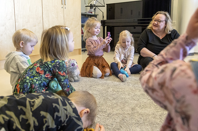 Lapsia ja yksi aikuinen istuu lattialla puoliympyrässä.
