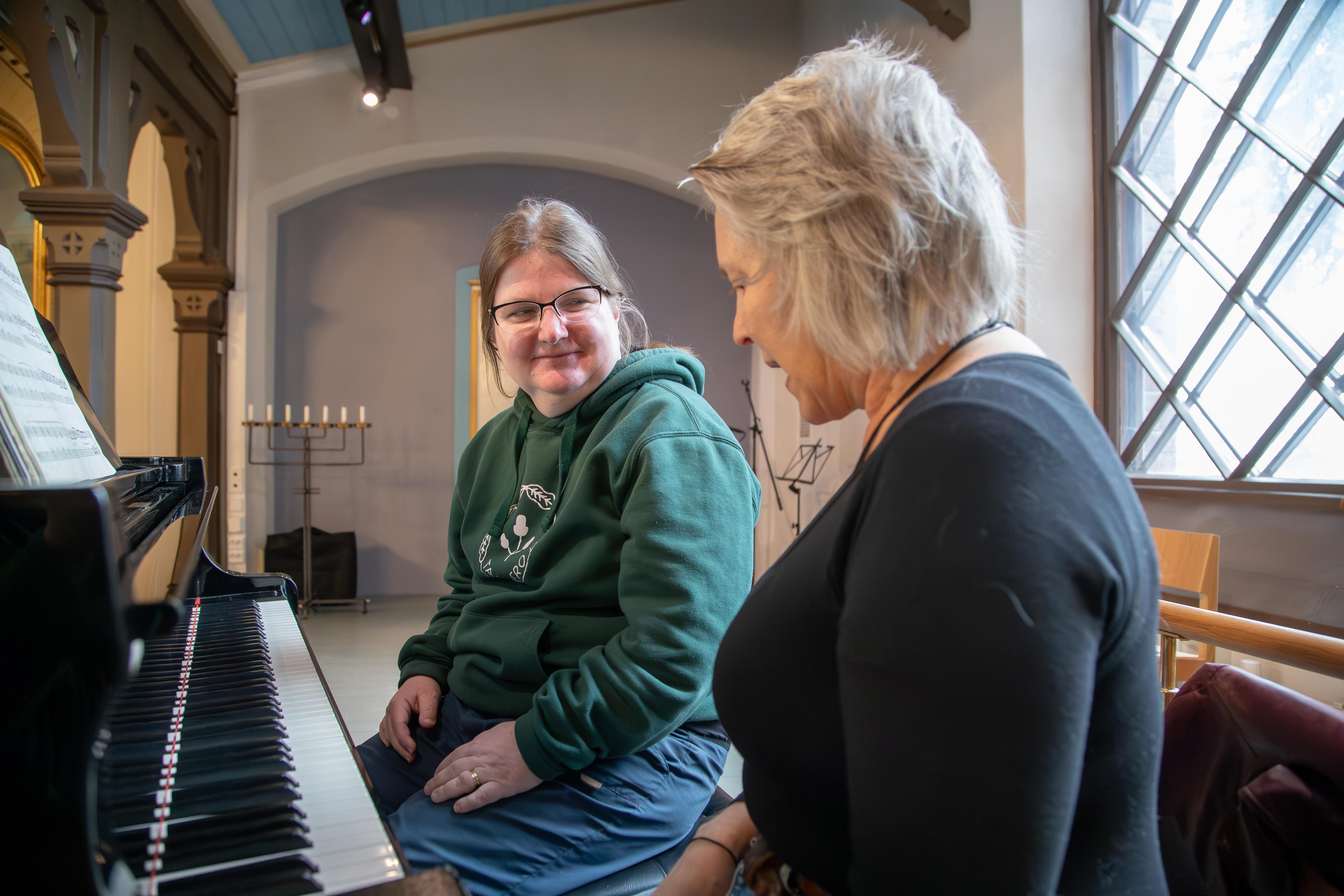 Kaksi ihmistä istuu pianon ääressä osittain toisiinsa päin kääntyneinä.