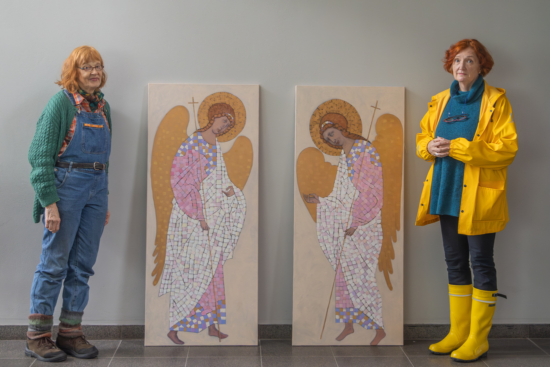 Kaksi naista seisoo kahden taulun sivuilla. Molemmissa tauluissa on kultasiipiset enkelit.