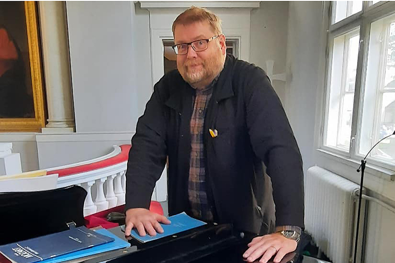 Mies nojaa kämmenillään alttarin lähellä olevaan pöytään, jonka päällä on nuottivihkoja.