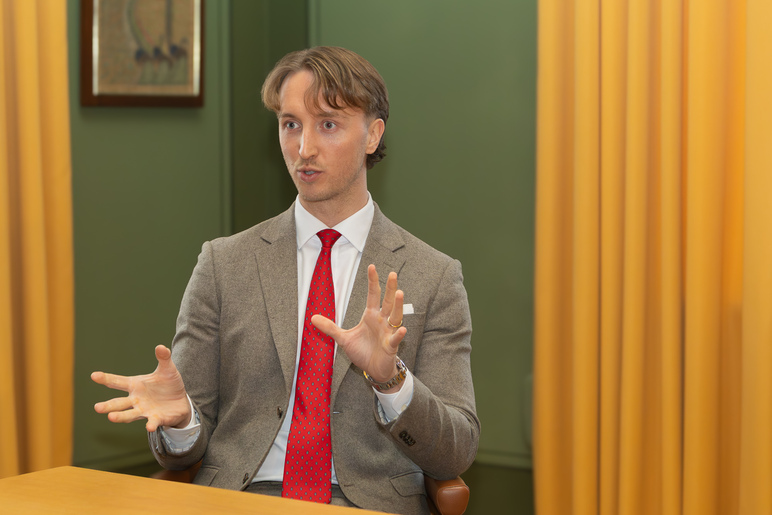 Mies istuu pöydän ääressä ja katsoo kamerasta pois päin.