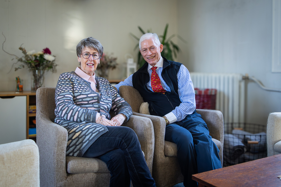 Nainen ja mies istuu kirkon taka-osassa nojatuoleilla ja hymyilevät kameralle.