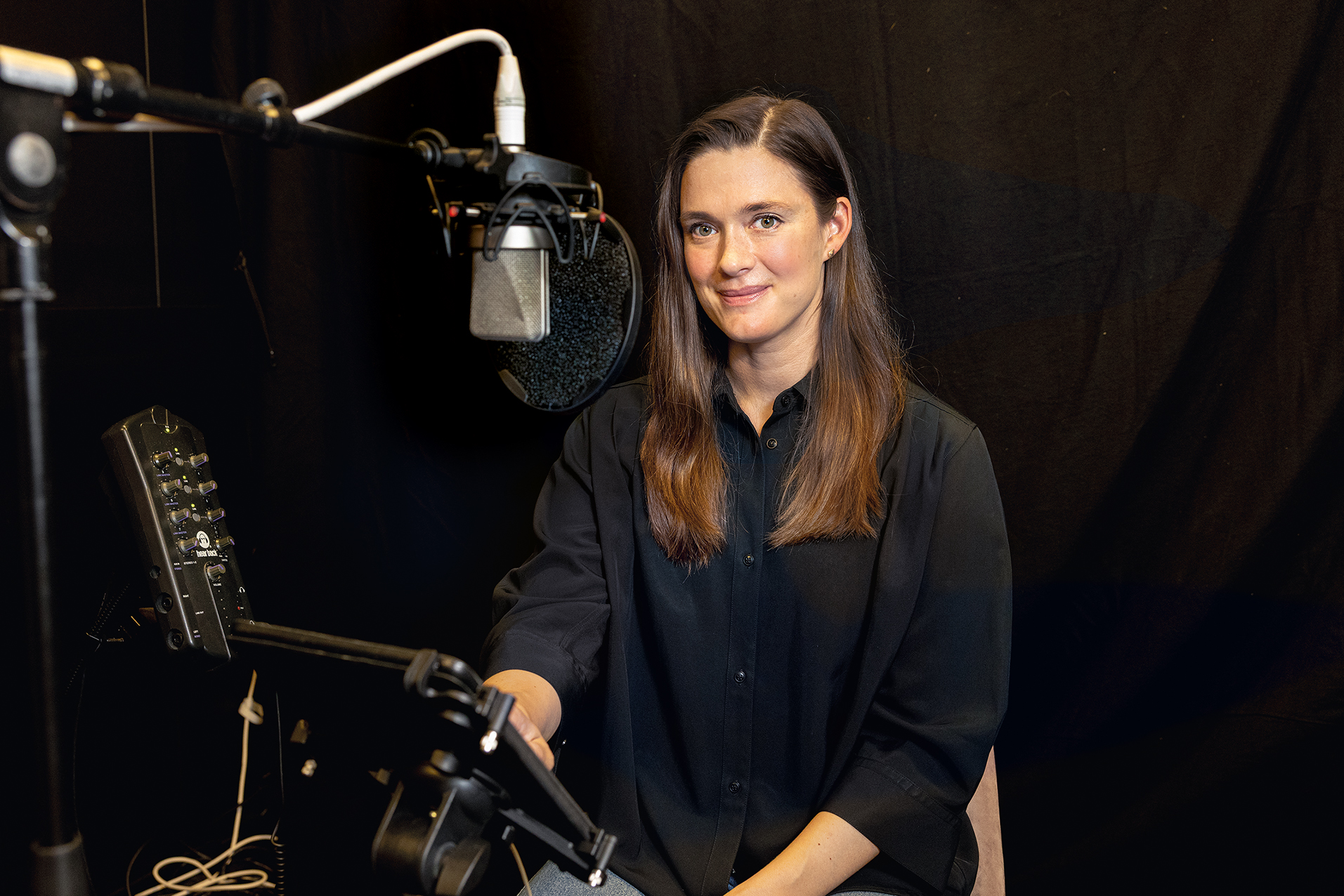 Nainen mustilla verhoilla sisutetussa studiossa mikrofonin kanssa.