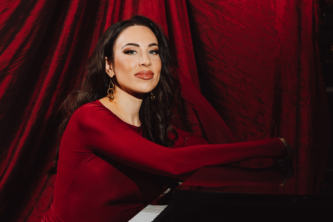 Nainen istuu flyygelin edessä punaisessa mekossa punaista taustaa vasten.