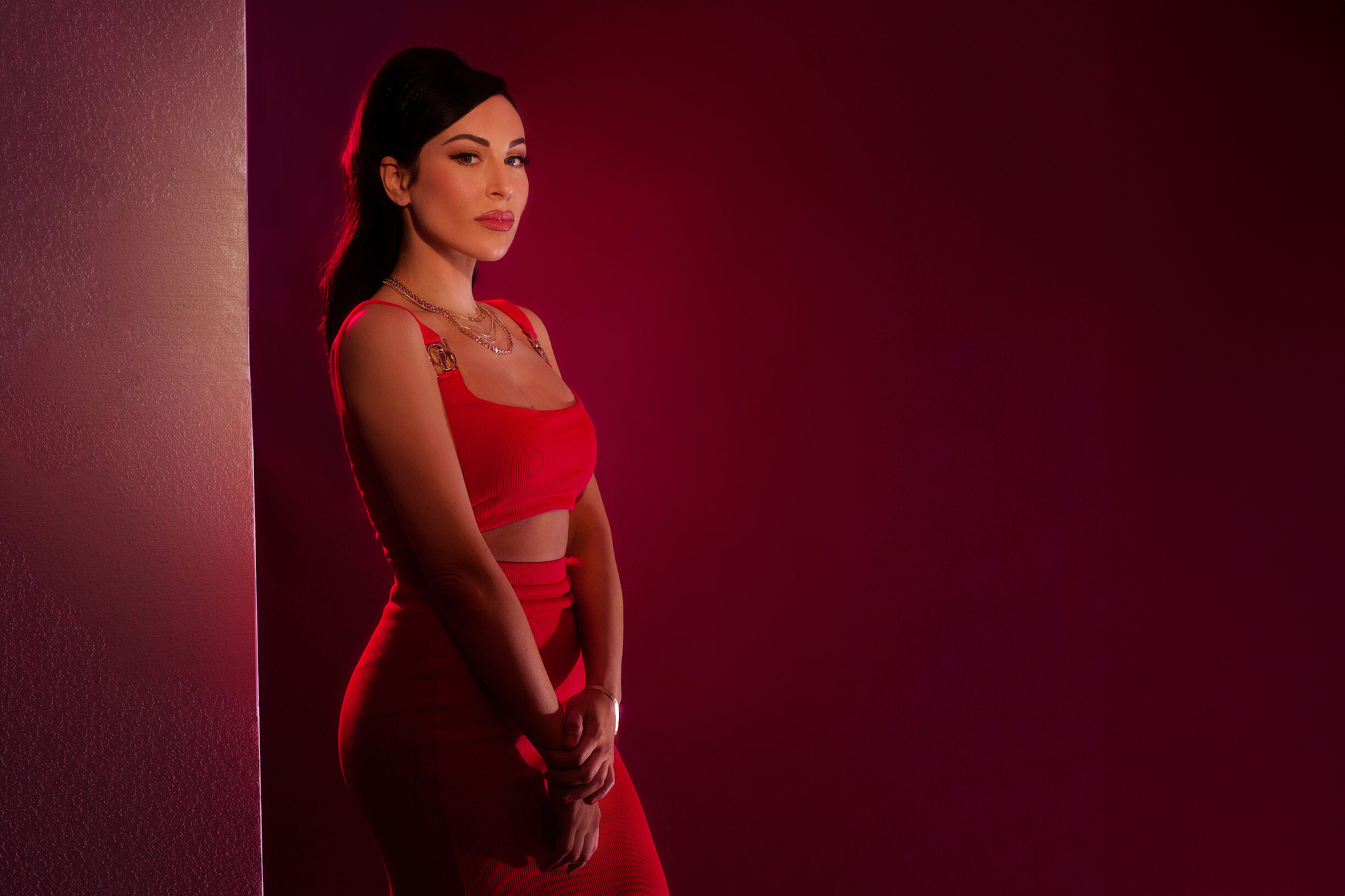 Nainen seisoo kylki kameraan päin punaista taustaa vasten.
