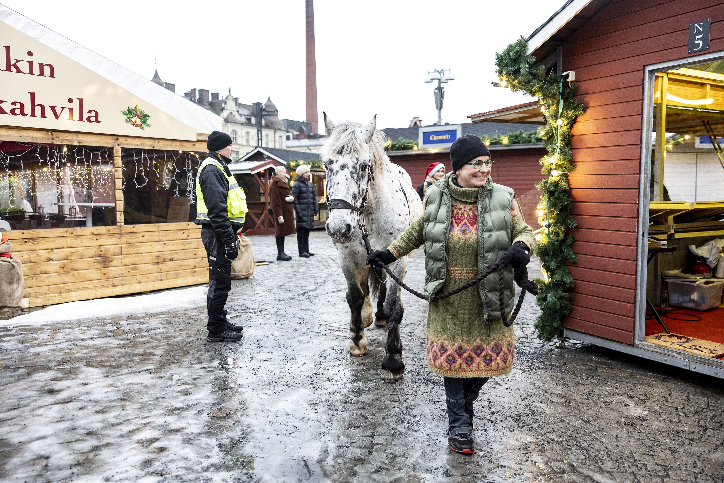 Hymyilevä nainen taluttaa hevosta kojujen keskellä.