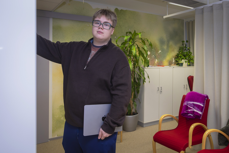 Toimistilassa seisova henkilö nojaa toisella kädellään seinään, ja alaspäin roikkuvassa kädessä on kannettava tietokone.