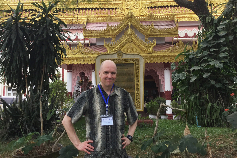 Henkilö seisoo kädet lanteilla kullanhehkuisen rakennuksen osan edessä.