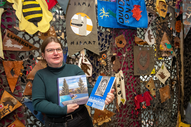 Nainen esittelee kahta kirjaa viirejä täynnä olevan seinän edessä.