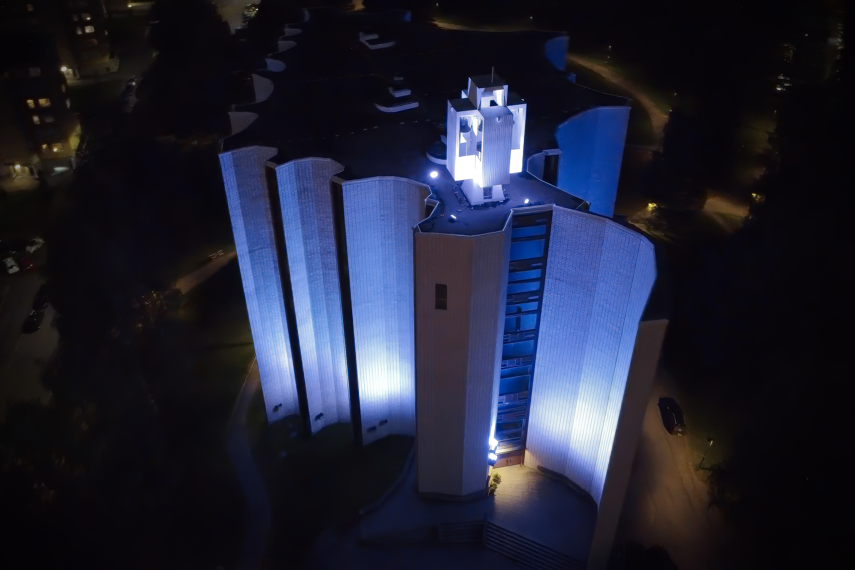 Yöllisessä näkymässä yläviistosta kuvattu jylhä iso rakennus, jossa on pystysuoria pylväsmäisiä seinärakenteita.