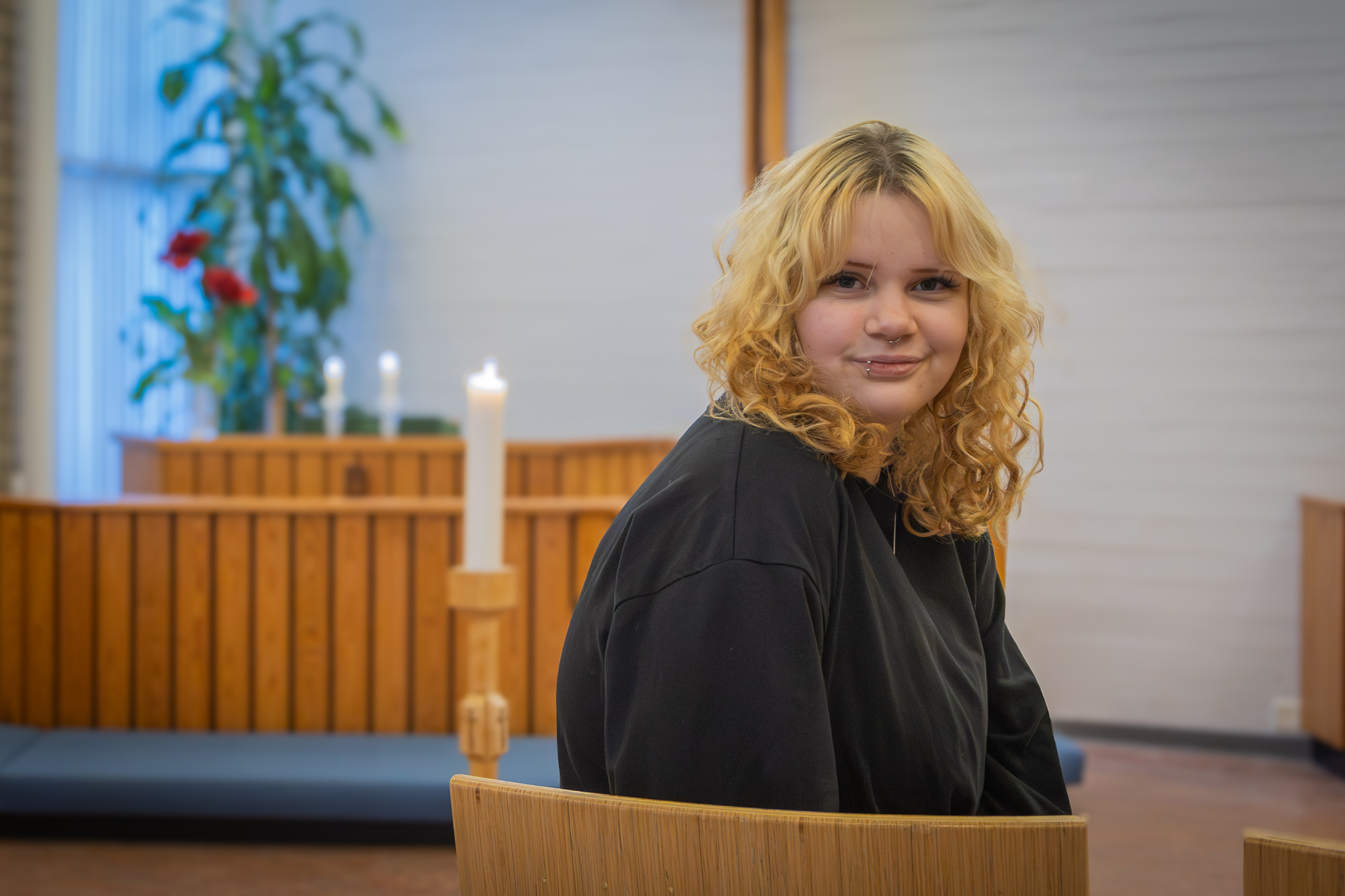 Puisen alttarin etupuolella puisella tuolilla istuu nuori nainen, joka on kääntynyt katsomaan taaksepäin.