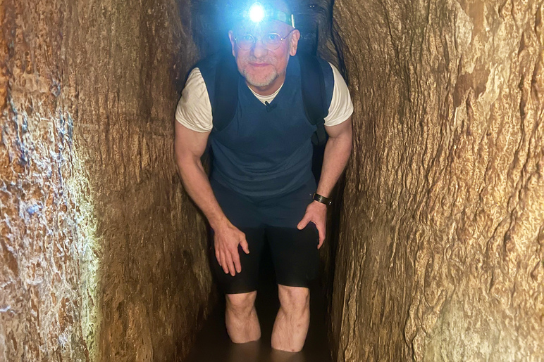 Henkilö kahlaa nilkkojaan myöten vedessä kahden seinämän välissä otsalamppu päässä.